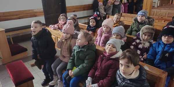 Dzieci siedzą w ławach kościelnych.