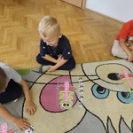 Dzieci siedzą na dywanie i układają papierowe owady przy kolorowej planszy z gąsienicą..jpg