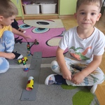 Dzieci siedzą na dywanie i bawią się własnoręcznie wykonanymi pojazdami na papierowej makiecie miasta..jpg