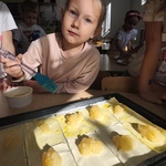 Dziewczynka przy pomocy pędzelka smaruje przygotowane kawałki ciasta_ na których znajduje się masa jabłkowa..jpg