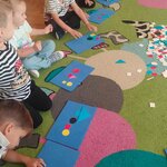 Dzieciom siedzą w kole i tworzą przestrzenne kompozycje z figur geometrycznych na podkładkach.jpg